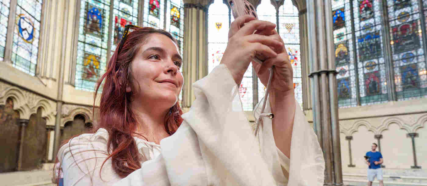 Visitor holding their phone looking at the multimedia guide and smiling standing in the Chapter House