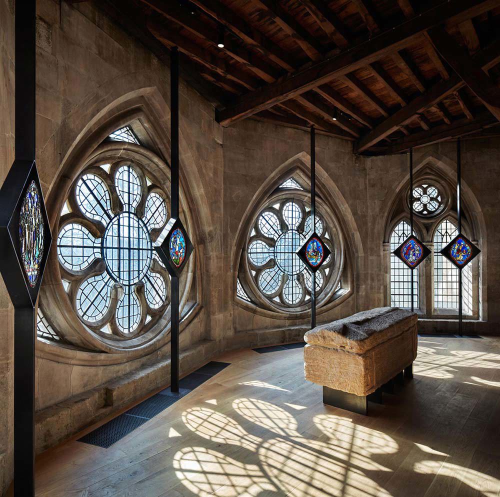 Ancient stone coffin on display with round stained glass windows and stained glass panels behind it