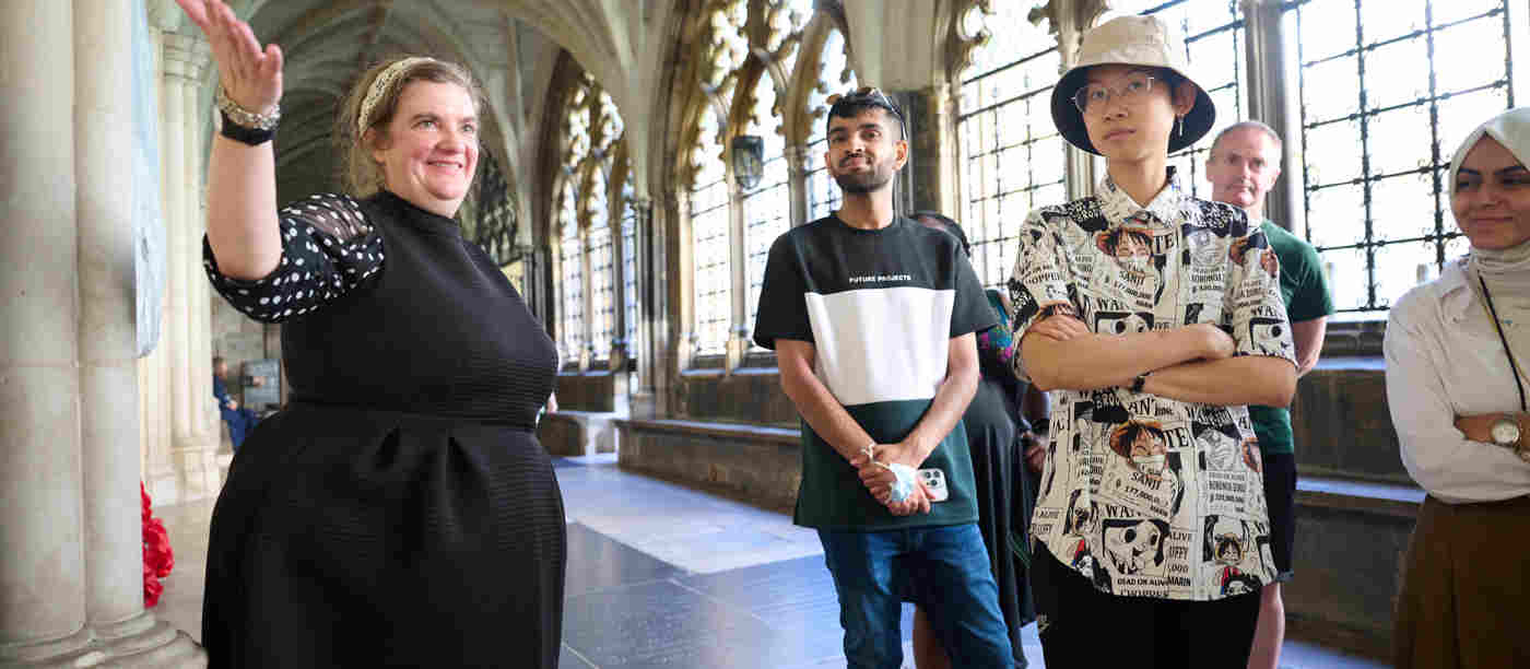 Photograph of female storyteller smiling and gesturing with other adults listening withing the cloisters of Westminster Abbey