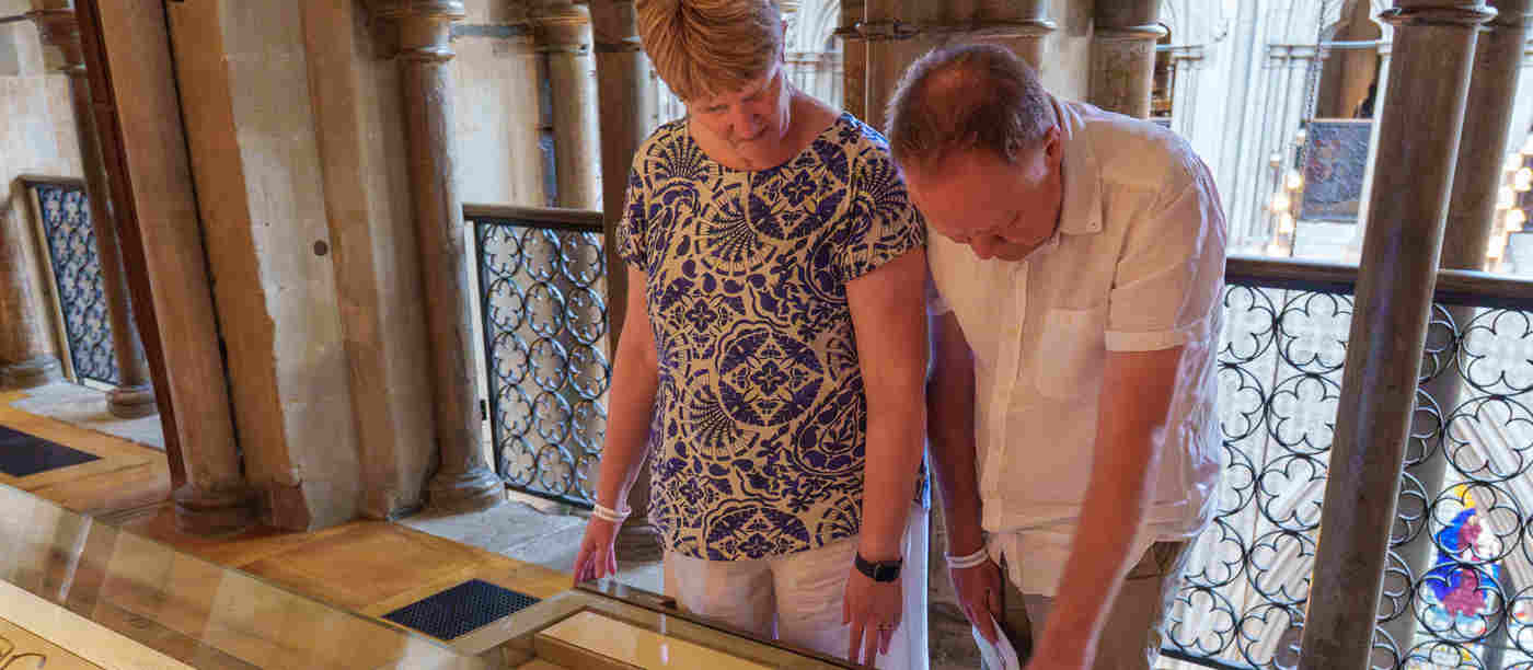 Photograph of two adults standing, looking down at a gallery case with historic objects within the Queen's Diamond Jubilee Galleries at Westminster Abbey