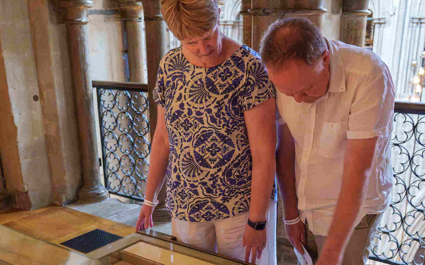 Photograph of two adults standing, looking down at a gallery case with historic objects within the Queen's Diamond Jubilee Galleries at Westminster Abbey