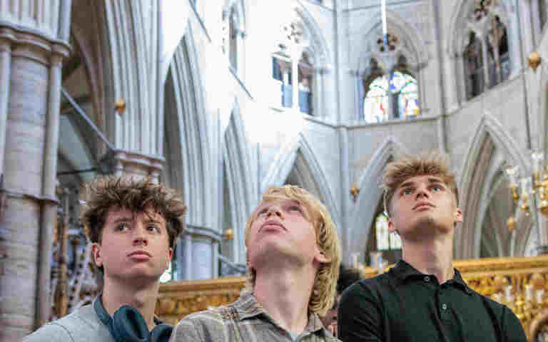 Photograph of three secondary school students looking up in different directions with the stone architecture of Westminster Abbey in the background