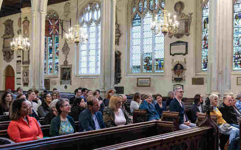 Photograph showing an audience of adults sitting in the pews of St Margaret's Church, Westminster Abbey listening to a talk