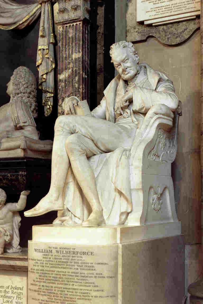 White marble statue of William Wilberforce seated in a chair with his legs crossed