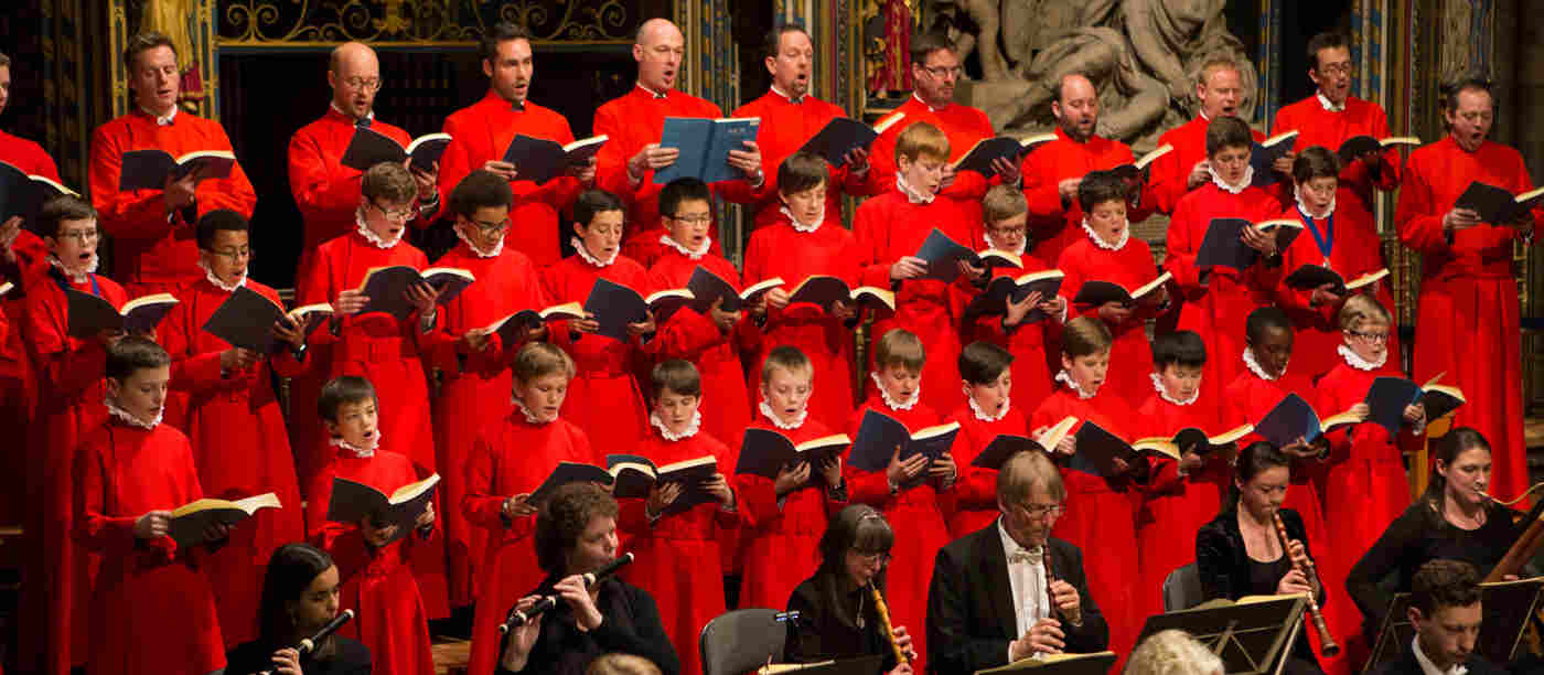 Photograph of Westminster Abbey Choristers, dressed in red robes, and an orchestra performing within the nave at Westminster Abbey