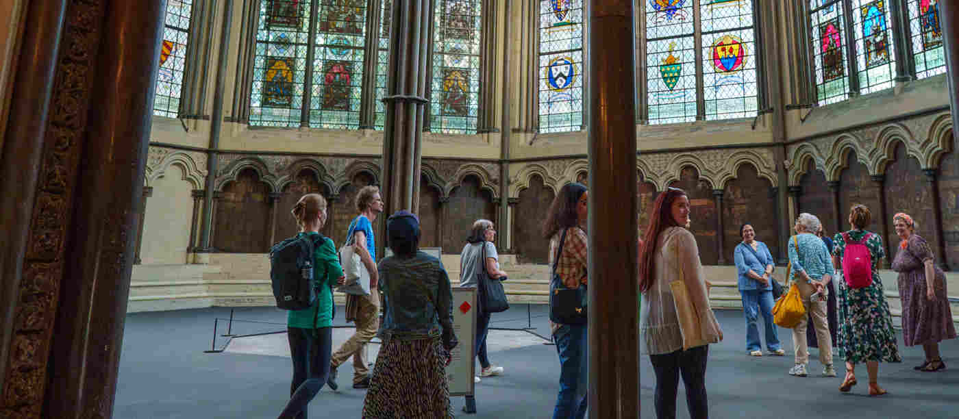 Photograph of people looking around the Chapter House, a space with medieval wall paintings and stained glass windows within Westminster Abbey