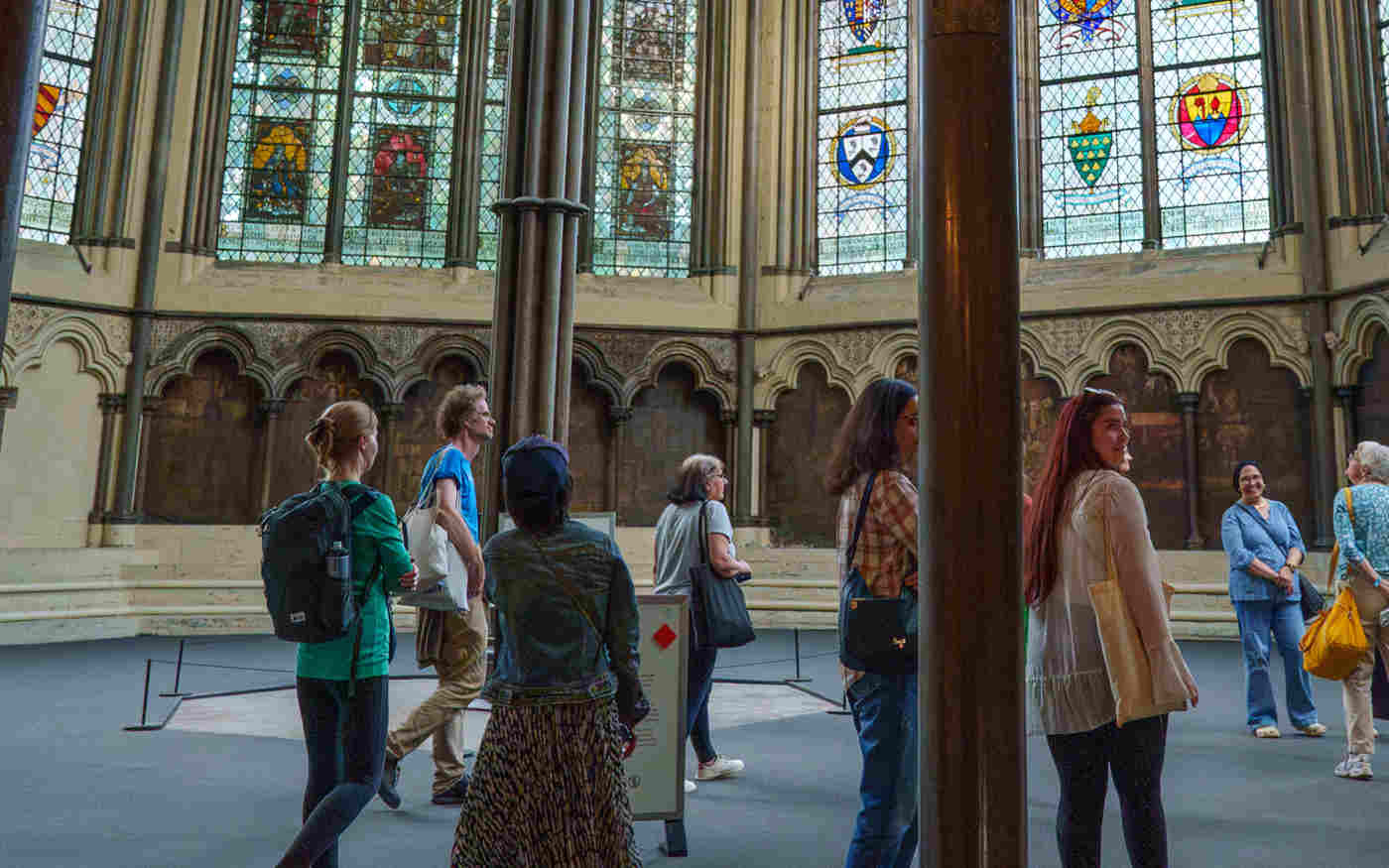 Photograph of people looking around the Chapter House, a space with medieval wall paintings and stained glass windows within Westminster Abbey