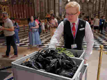 Photograph of male visitor experience assistant pushing a trolley of multimedia guides through Westminster Abbey