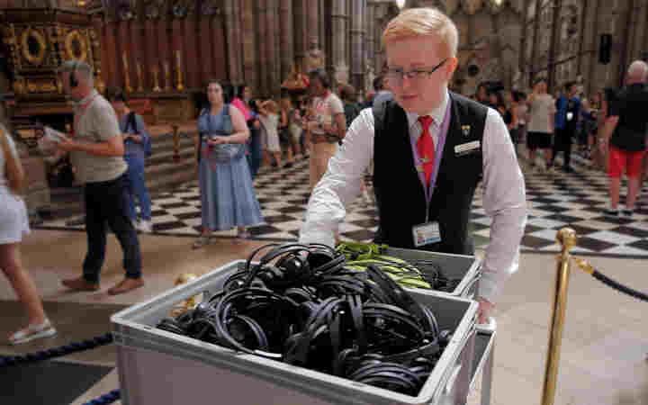 Photograph of male visitor experience assistant pushing a trolley of multimedia guides through Westminster Abbey