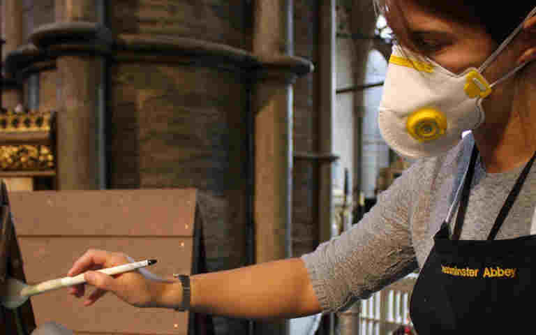 Photograph of a female member of the conservation team, wearing a mask, brushing clean a pointed internal roof