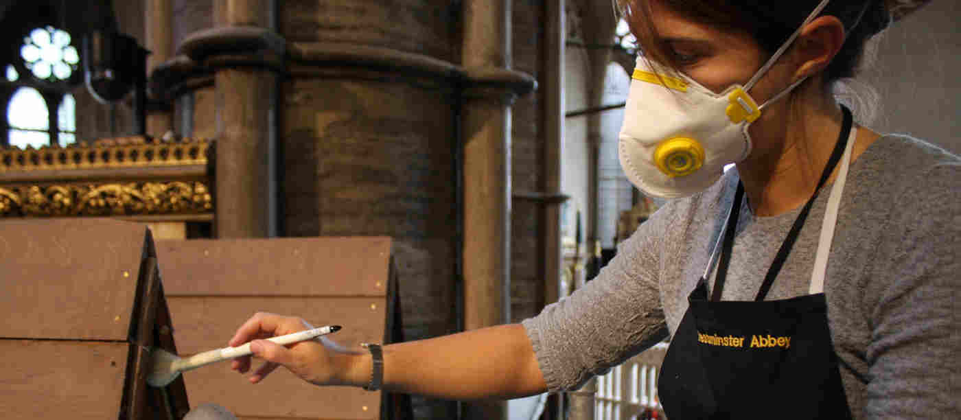 Photograph of a female member of the conservation team, wearing a mask, brushing clean a pointed internal roof
