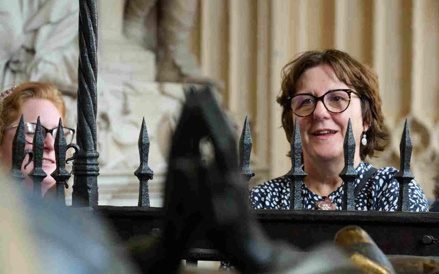Photograph of women looking at tomb surrounding by rails in Westminster Abbey