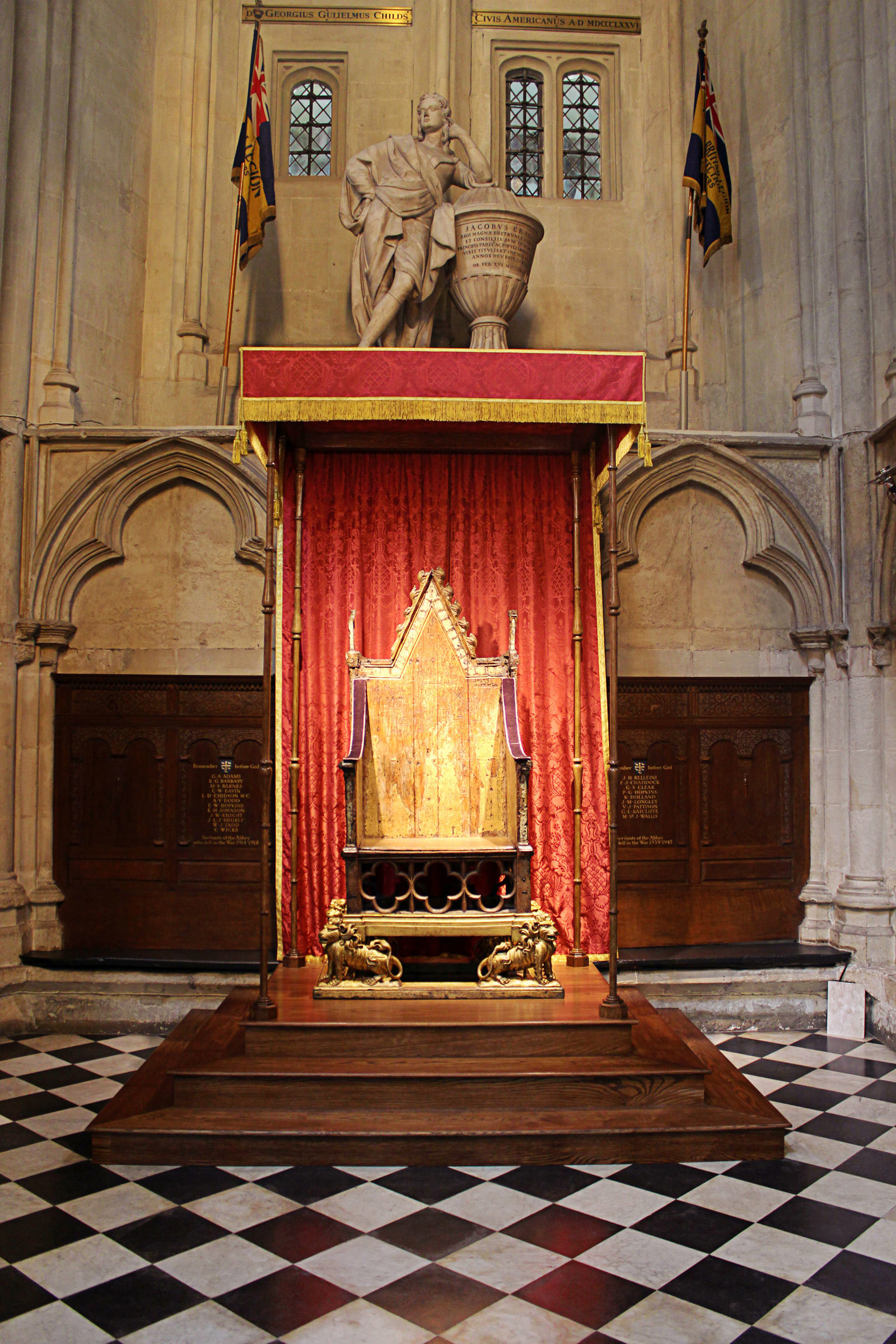 The Coronation chair on a stepped wooden podium with flags and a statue set into the wall above