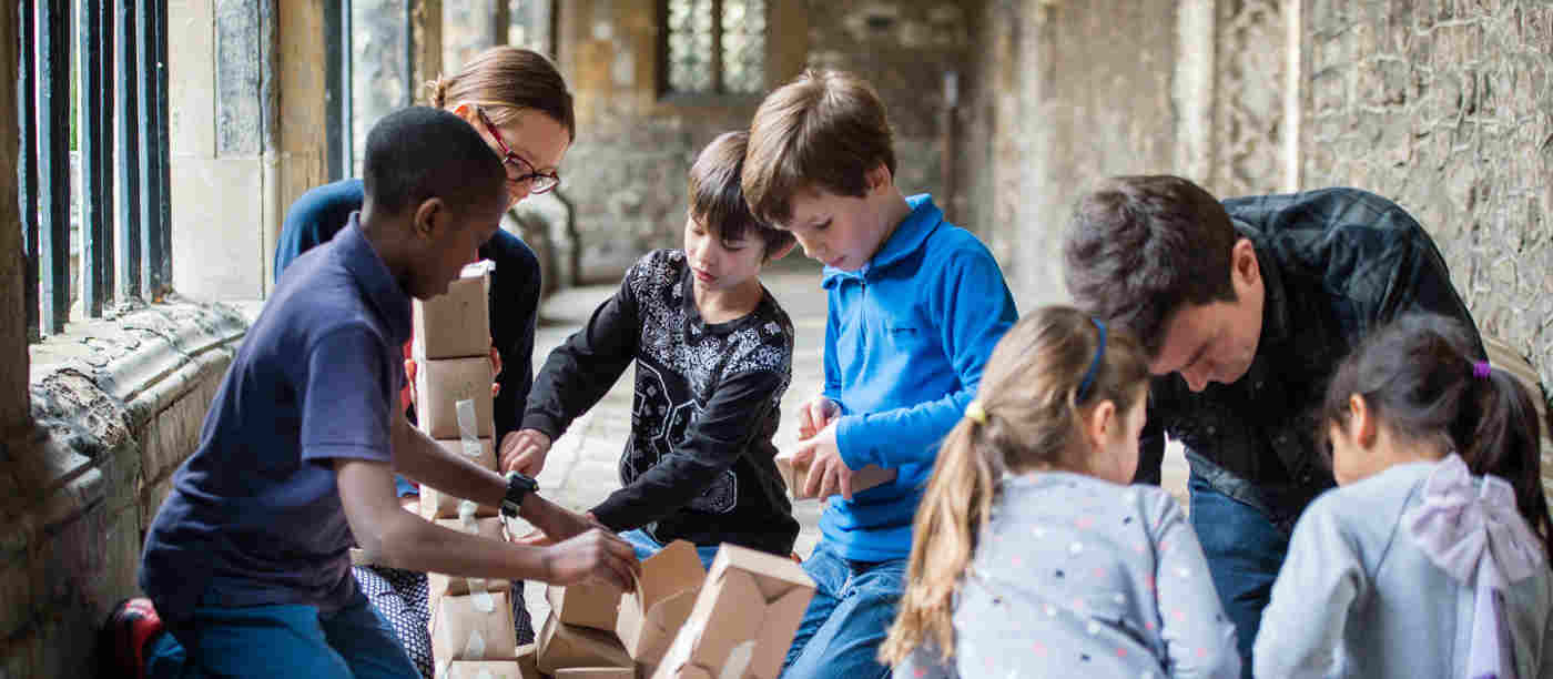 Photograph of groups of families working together to build objects out of cardboard in the cloisters of Westminster Abbey