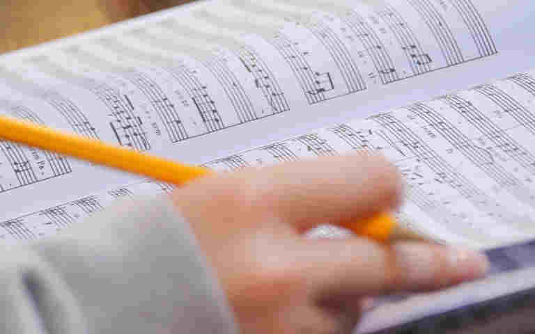 Close-up photograph of a music score and a choristers hand holding a pencil