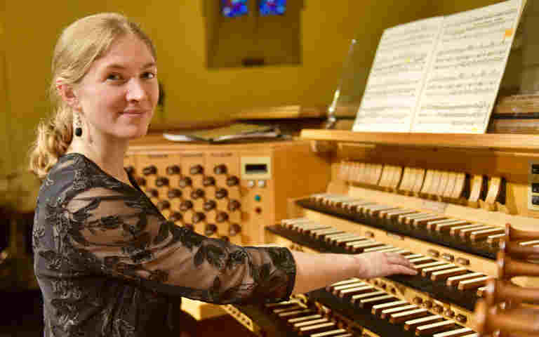 Photograph of organist Carolyn Craig, currently the Organ Scholar at Westminster Abbey, sitting at an organ ready to play, looking at the camera