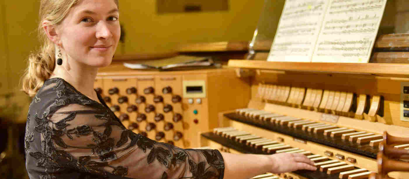 Photograph of organist Carolyn Craig, currently the Organ Scholar at Westminster Abbey, sitting at an organ ready to play, looking at the camera