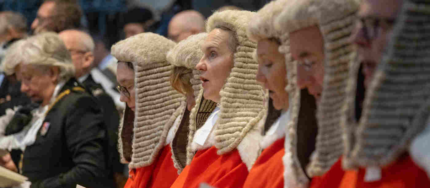 Judges in red robes and legal wigs reading from hymn sheets