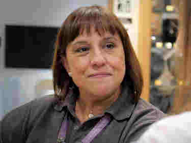 Photograph of woman in grey uniform smiling at a customer within Westminster Abbey's Shop