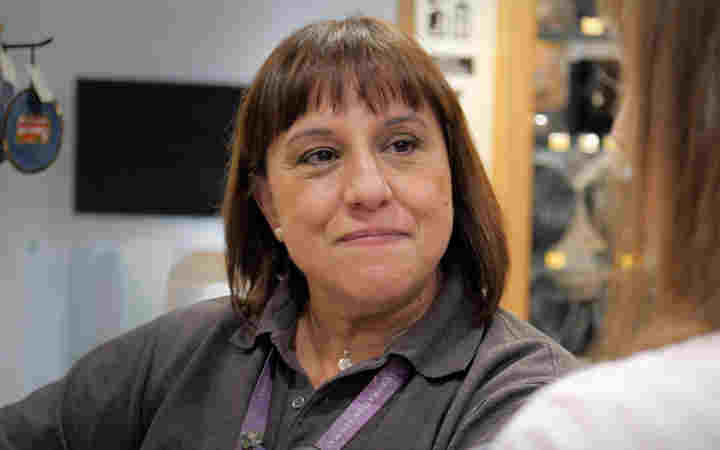 Photograph of woman in grey uniform smiling at a customer within Westminster Abbey's Shop