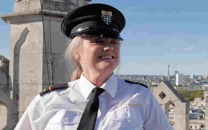 Photograph of smiling female security beadle wearing uniform, looking at from the top of the flag tower at Westminster Abbey