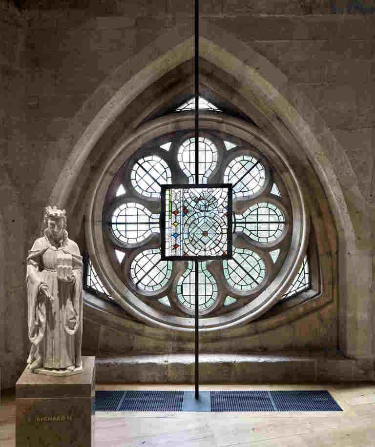 Small white statue of Richard III with a stained glass panel and a round stained glass window behind it