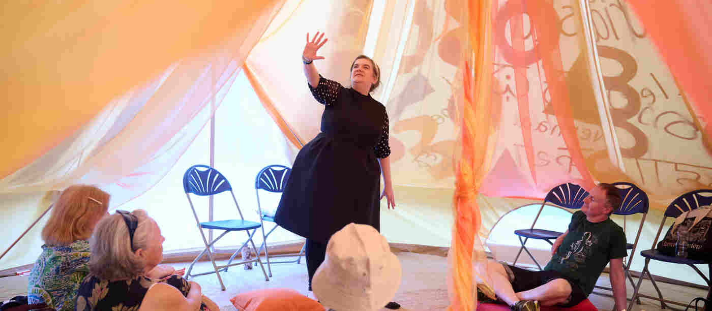 Photograph of storyteller standing within a canvas tent, performing to an adult audience at Westminster Abbey