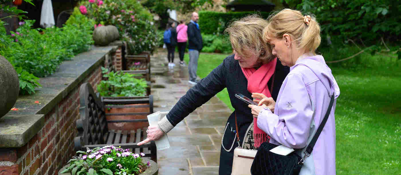 Photograph of two members of the public talking and pointing at flowers in College Garden at Westminster Abbey