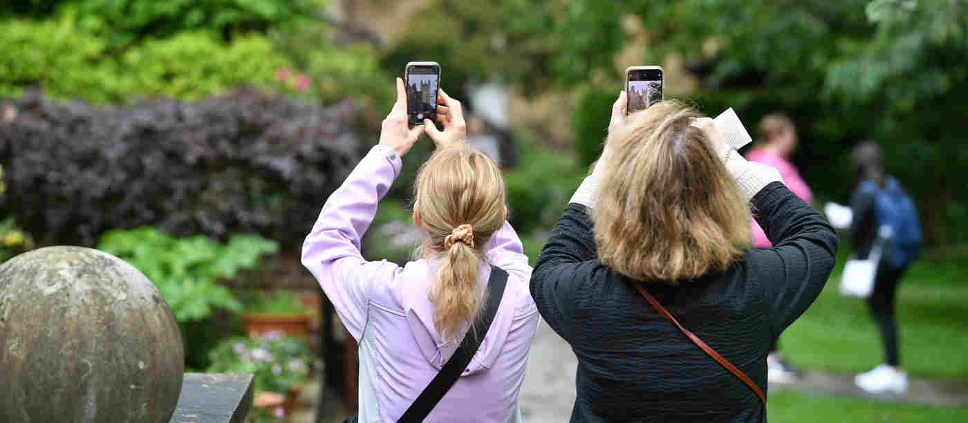 Photograph of the back of two tourists taken photographs with their phones standing within College Garden in Westminster Abbey
