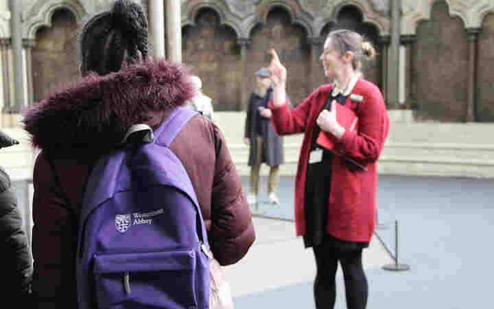 Photograph of the back of a student carrying a purple sensory backpack, with a member of staff delivering a talk in the background within the Chapter House