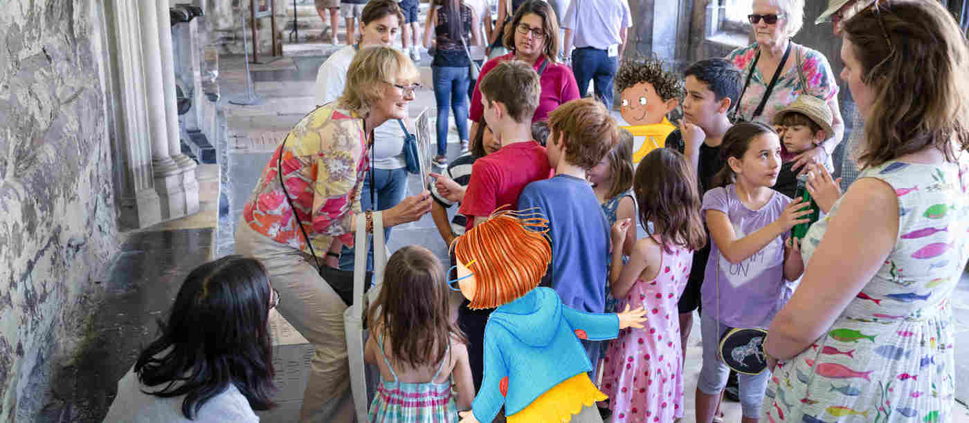 Photograph of an adult leading a tour for children and adults in the cloisters of Westminster Abbey including an illustrated child