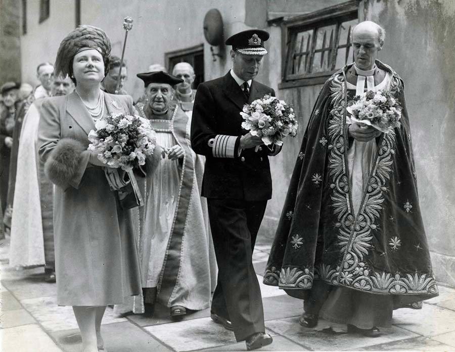 Queen Elizabeth, George VI and the Dean of Westminster lead a procession holding bunches of flowers