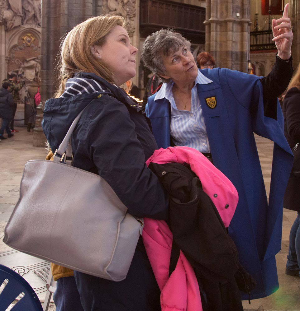 A volunteer Westminster Abbey Guide explains a feature of the church to a visitor
