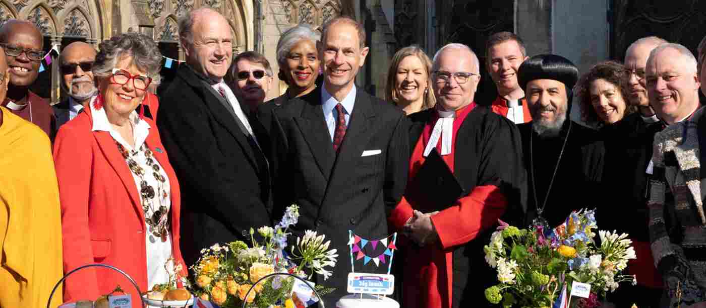 Prince Edward, David Hoyle, Prue Leith and faith leaders standing in front of a table featuring cake and quiche.