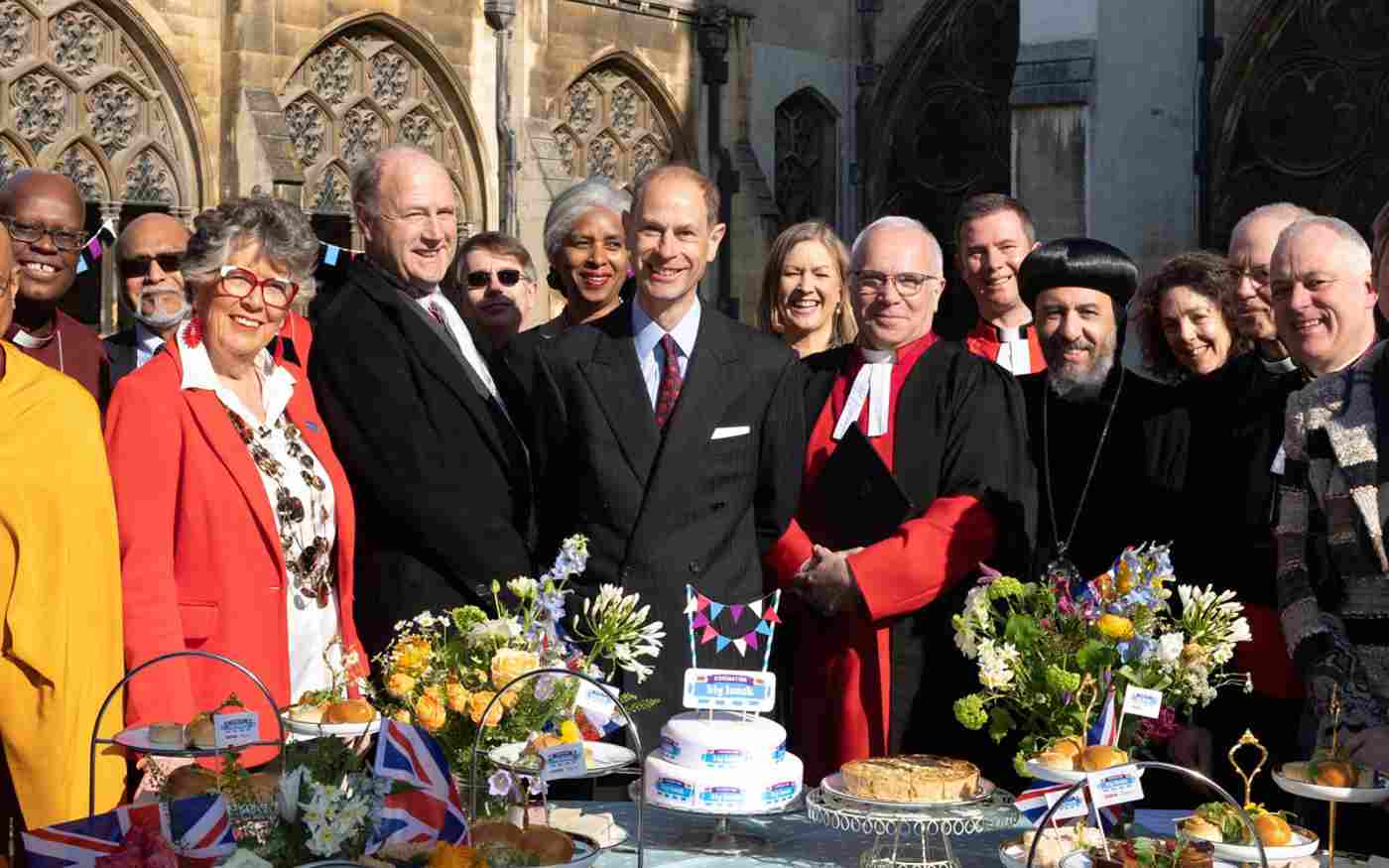 Prince Edward, David Hoyle, Prue Leith and faith leaders standing in front of a table featuring cake and quiche.