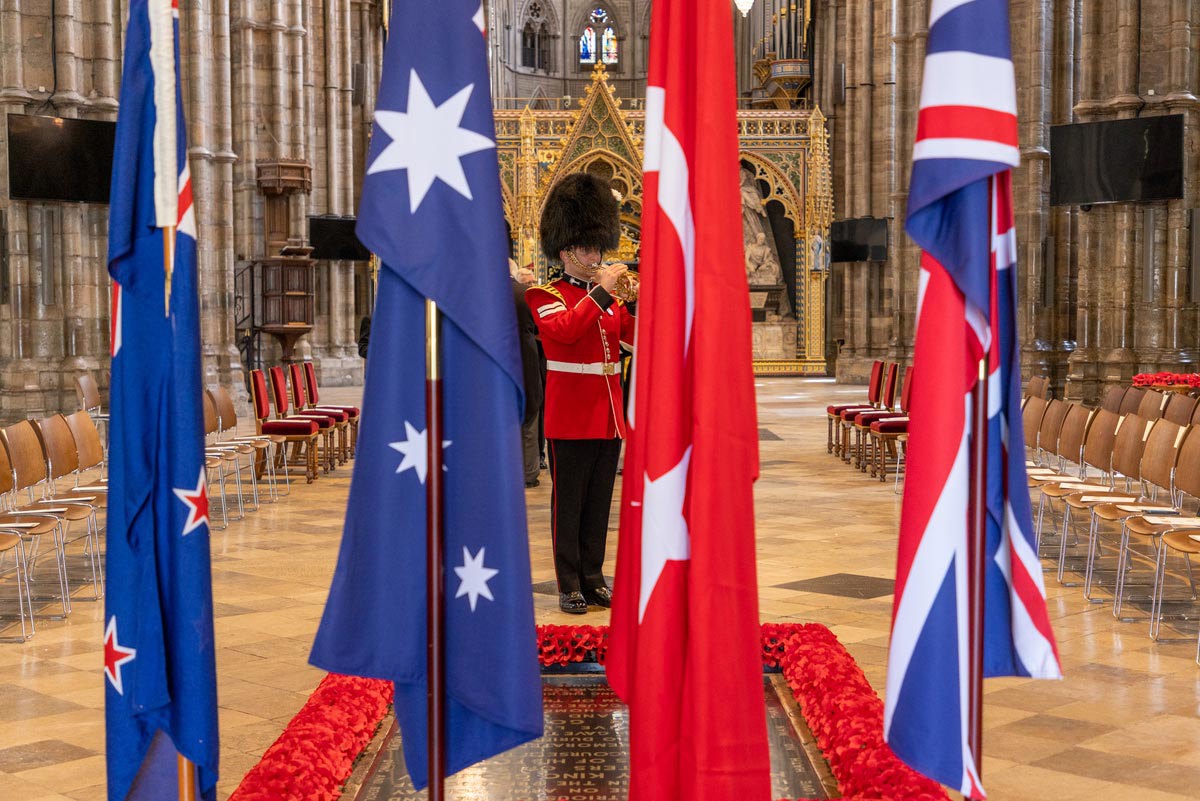 A soldier plays the trumpet by the Grave of the Unknown Warrior. Flags of Australia, New Zealand, Turkey and the UK are in the foreground