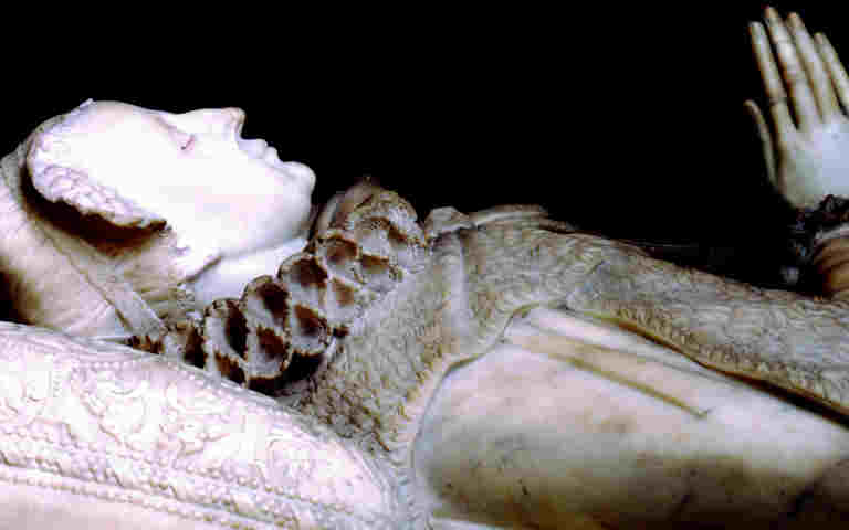 White marble effigy of Mary Queen of Scots lying down, with her head resting on a patterned cushion and her hands in the prayer position
