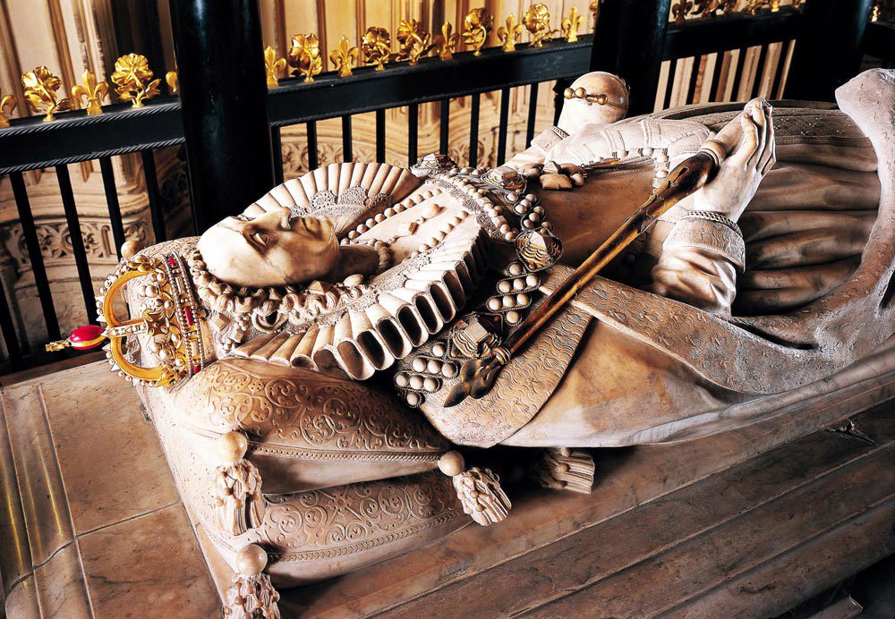 White marble tomb effigy of Elizabeth I wearing a crown and holding a sceptre and orb
