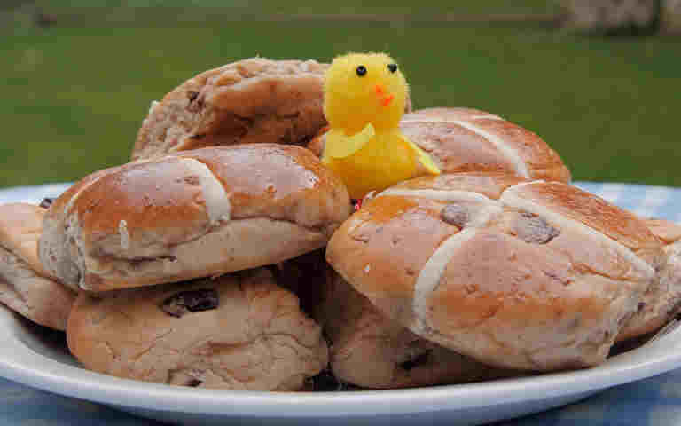 Photograph of yellow chick sitting in a plate of hot cross buns in a garden in Westminster Abbey