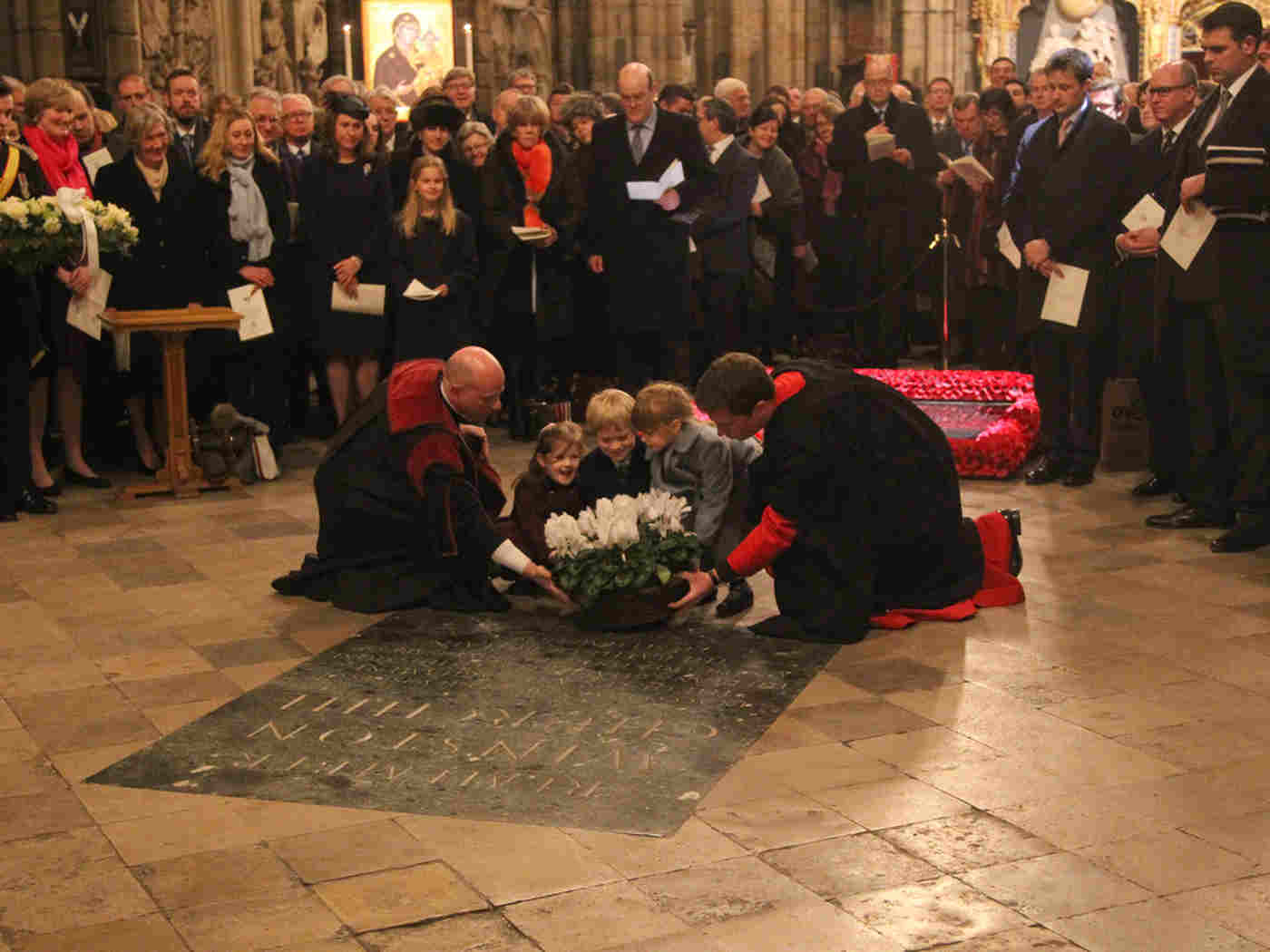 Iona Pite, John Winston Churchill, and Christabel Fraser, great-great-grandchildren, are helped to lay their flowers on the memorial of Sir Winston Churchill in the Nave