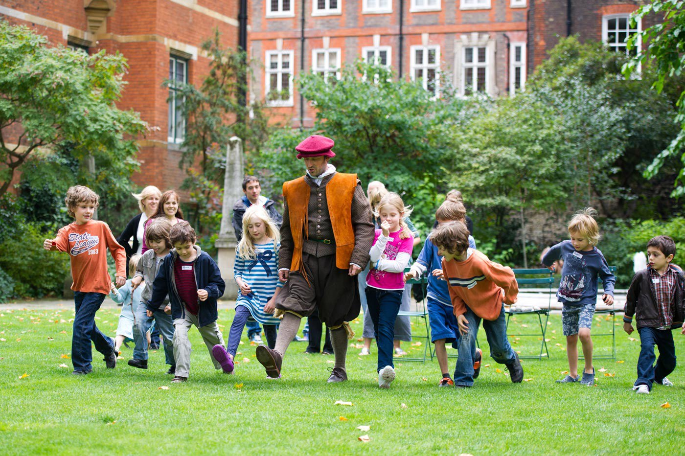 A man in medieval costume walks with a group of children through College Garden, Westminster Abbey