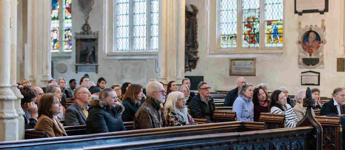 Photograph showing an audience of adults sitting in the pews of St Margaret's Church, Westminster Abbey listening to a talk