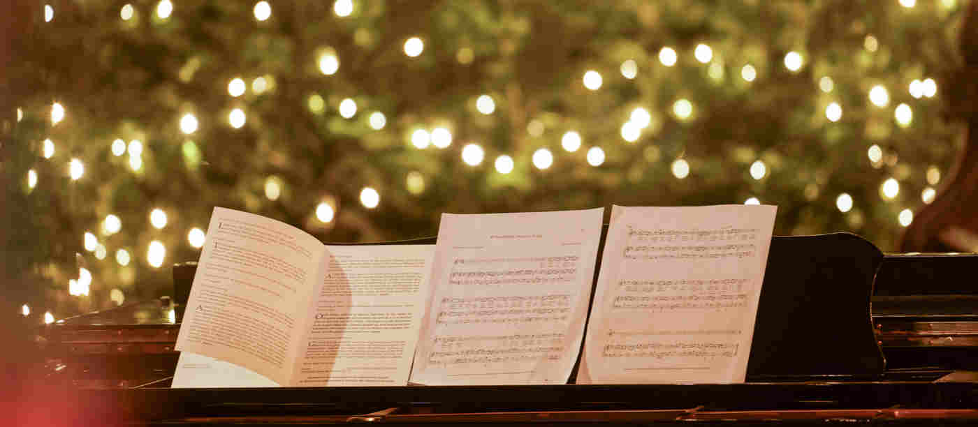 Photograph of a piano with four pages of sheet music and in the background a lit Christmas tree filling the whole space
