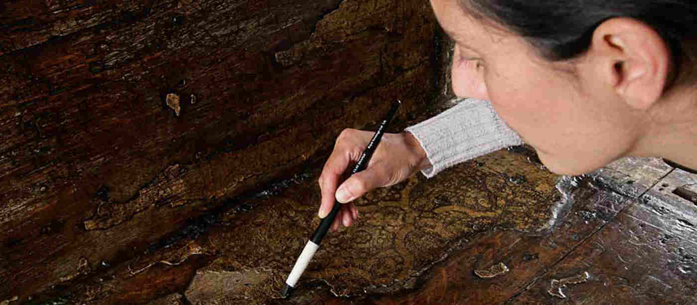 Photograph of a female member of the conservation team using a brush on a wooden object