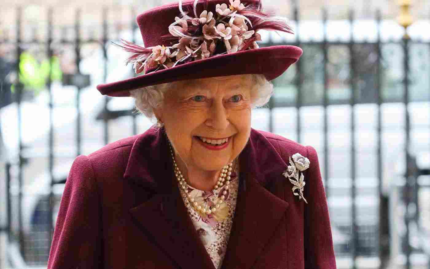 Elizabeth II wearing a maroon jacket, pink floral blouse and maroon hat decorated with pink flowers