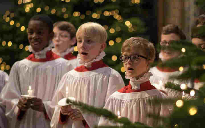 Photograph of Westminster Abbey choristers holding candles singing at Christmas, with a Christmas tree in the bottom right hand corner,