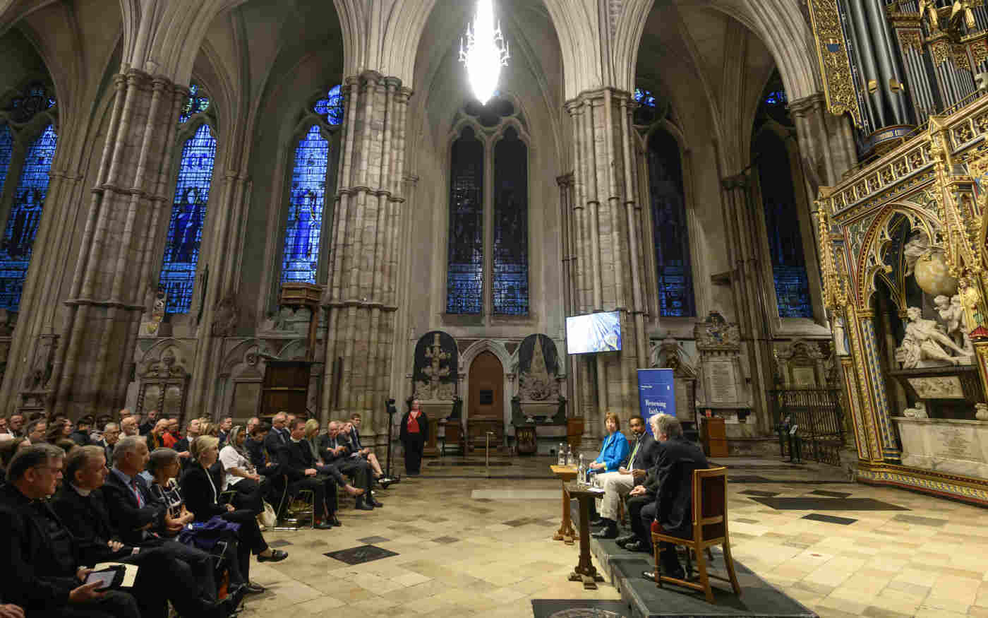 Photograph from the side of a panel discussion with the audience listening within the nave of Westminster Abbey