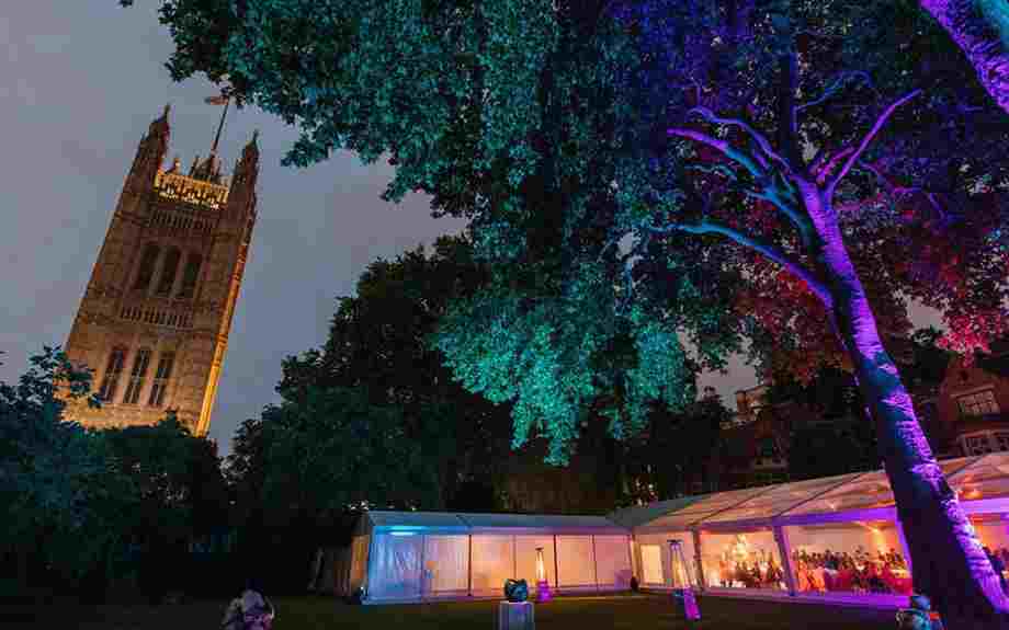 Glass marquee in Westminster Abbey's College Garden at night, lit up with colourful lights