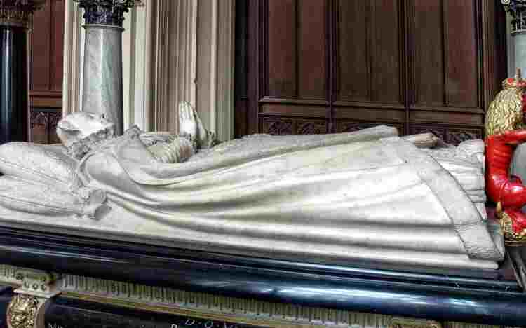 Recumbent marble effigy of Mary Queen of Scots, her hands raised in prayer, a red lion at her feet