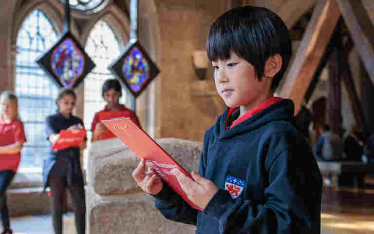 Photograph of child in uniform holding a red clipboard within Westminster Abbey